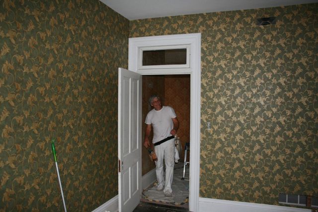 A finished interior room in patterned wallpaper with a painter in the doorway
