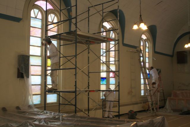 Painters on scaffolding painting the interior of a tall arched-window hall