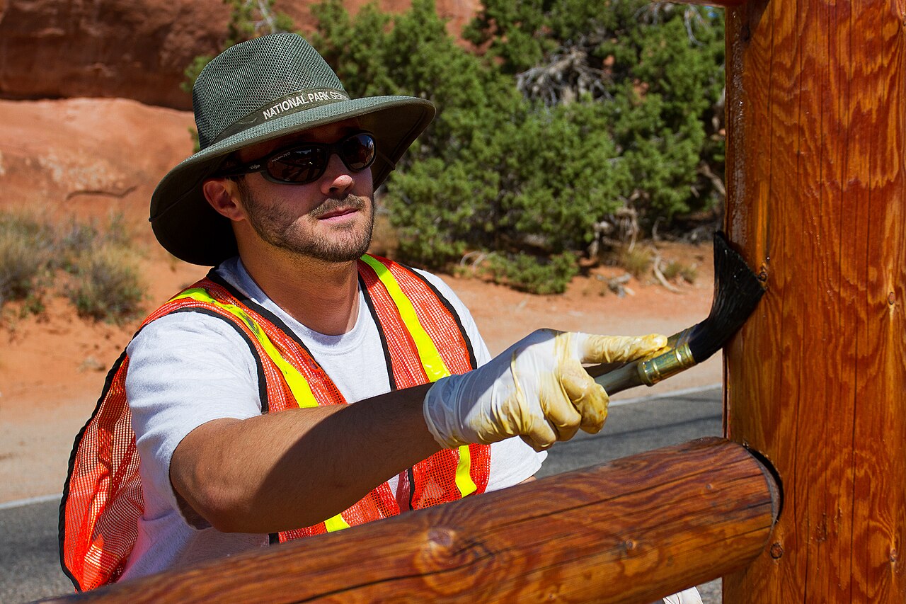 A worker brushing stain onto a wooden fence