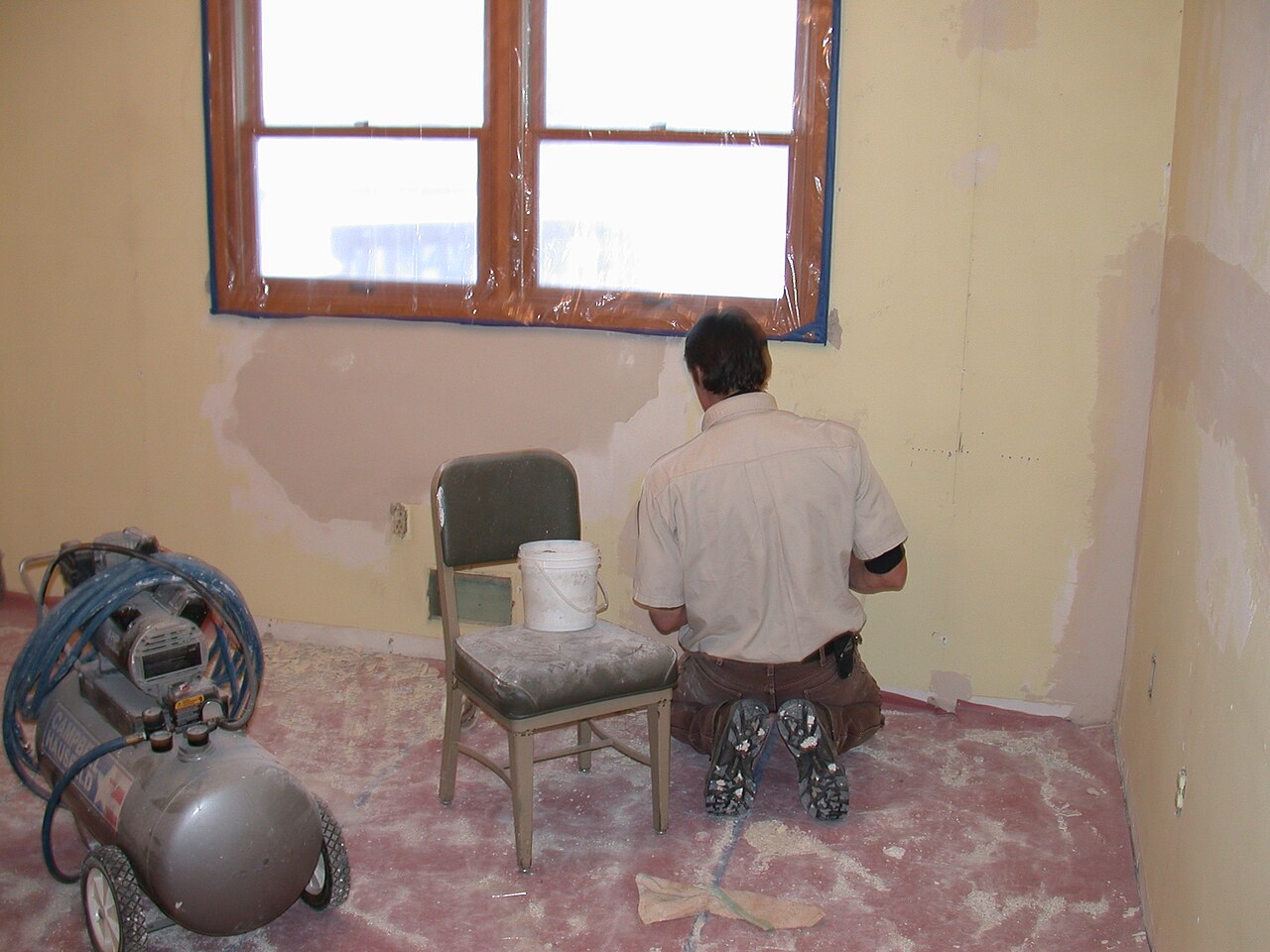 A worker repairing a drywall wall in a room being refinished